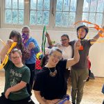 Group of young adults with additional needs and course leader all dancing, smiling and moving with joy. Representing well being for people with learning disabilities and their carers