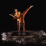 Contemporary circus performers balancing a wine glass during an acrobatic handstand act on a dark stage, showcasing balance, strength and live performance art