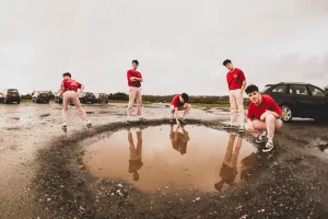 Boss Cass press photo showing the musician in multiple poses around a large puddle in an outdoor car park.