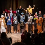 Community theatre cast taking a bow after a live stage performance in costume, with the audience applauding. Ideal for promoting inclusive theatre, amateur drama and live performance events.