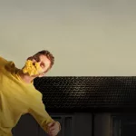 Dance theatre production image showing a man in a yellow sweater with flowers covering his face, representing childhood trauma, resilience, healing, and emotional recovery.